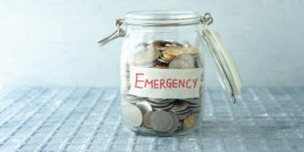 Coins in glass money jar with emergency label, financial concept.